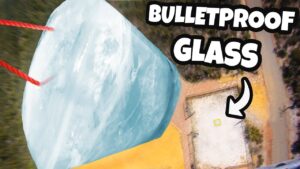 Large, pale-blue glass block suspended by red ropes, viewed from above, with bold 'BULLETPROOF GLASS' text in the corner.