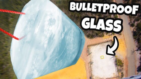 Large, pale-blue glass block suspended by red ropes, viewed from above, with bold 'BULLETPROOF GLASS' text in the corner.