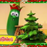 Cartoon VeggieTales scene: a tall green vegetable with a red hat stands beside a decorated Christmas tree inside a festive frame, with the VeggieTales logo bottom-left.