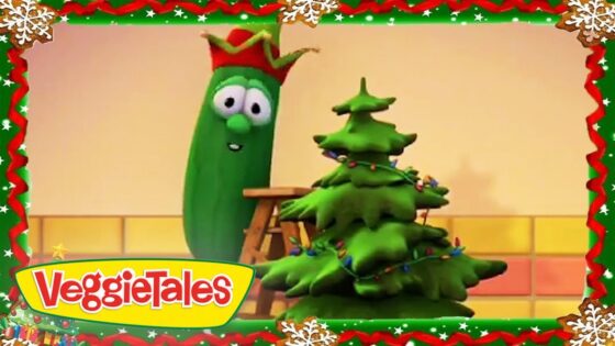 Cartoon VeggieTales scene: a tall green vegetable with a red hat stands beside a decorated Christmas tree inside a festive frame, with the VeggieTales logo bottom-left.