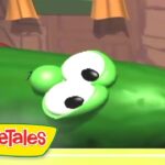Green cucumber character with big white eyes lying on its side in a VeggieTales scene.