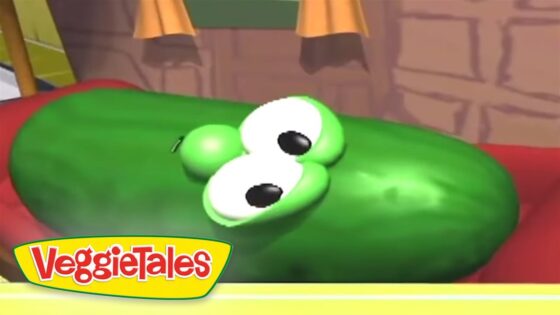 Green cucumber character with big white eyes lying on its side in a VeggieTales scene.