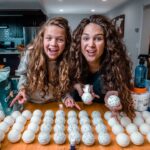Two girls smiling at a kitchen table with rows of hollow eggshells, crafting speckled egg decorations.