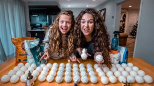 Two girls smiling at a kitchen table with rows of hollow eggshells, crafting speckled egg decorations.