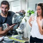 Man operating a circular saw while a woman nearby looks surprised and happy in a home workshop.