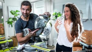 Man operating a circular saw while a woman nearby looks surprised and happy in a home workshop.
