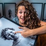 Woman with curly hair holding a large framed photo of a smiling child, and is pointing at the image.