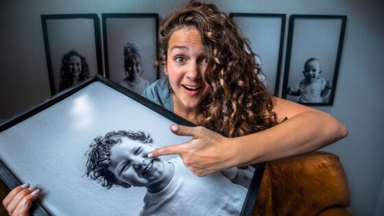 Woman with curly hair holding a large framed photo of a smiling child, and is pointing at the image.