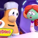 Two VeggieTales characters sit at a table; one holds a plate with a hot dog while the green, red-haired character looks on with surprise.