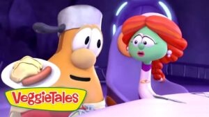 Two VeggieTales characters sit at a table; one holds a plate with a hot dog while the green, red-haired character looks on with surprise.