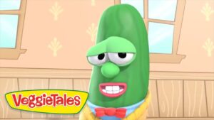 Sleepy green cucumber character in a VeggieTales scene, wearing a red bow tie in a wooden-room setting.