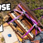 Piano strapped with purple lifting straps being hoisted from a rooftop, with a man shouting from a balcony wearing sunglasses.