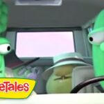 Two VeggieTales characters—a broccoli-headed figure with glasses and a tall green cucumber—sit in a car with a passenger in a hat; logo in corner.