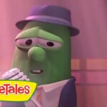 Green VeggieTales character in a suit and hat singing into a microphone on stage, VeggieTales logo visible in the corner
