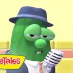 Green cucumber character in a hat and suit sings into a vintage microphone on a stage, with the VeggieTales logo in the corner.