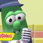 Green veggie character in a blue hat sings into a retro microphone on a pastel stage; VeggieTales logo visible in the corner.