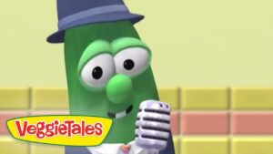 Green veggie character in a blue hat sings into a retro microphone on a pastel stage; VeggieTales logo visible in the corner.