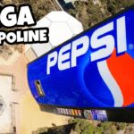 Aerial view of a large blue Pepsi sign on a tall amusement ride with bold 'MEGA TRAMPOLINE' text overlay.