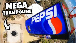 Aerial view of a large blue Pepsi sign on a tall amusement ride with bold 'MEGA TRAMPOLINE' text overlay.