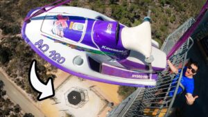Thrill ride scene: a purple Kawasaki jet ski is mounted above a platform while a man in blue stands on the railing, giving a thumbs-up.