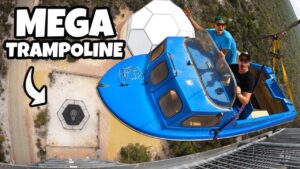 Thumbnail for a mega trampoline stunt: two men in a blue ride capsule yelling as it’s hoisted by a crane high above the ground.