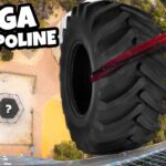 Thumbnail of a man in sunglasses on a high railing, gripping a giant tire attached to cords for a 'mega trampoline' stunt, with a hexagonal landing pad on the ground marked by a question mark and a bold arrow.