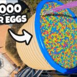 Aerial view of a blue tub full of colorful Easter eggs on a platform, with two excited men nearby and a bold '100,000 Easter Eggs' banner text.
