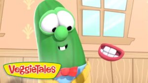 Green cucumber character with large eyes and a red bow tie talking to a floating red lips prop, in a cozy wooden room; VeggieTales logo in corner.