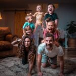 A family of six posing in a playful human pyramid in their living room, smiling at the camera.