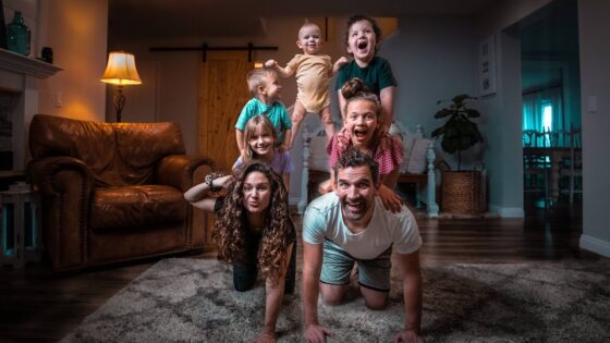 A family of six posing in a playful human pyramid in their living room, smiling at the camera.