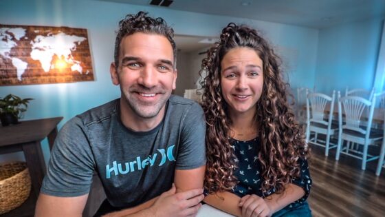 Smiling man and woman sit at a table in a bright, modern room with world map wall art behind them.