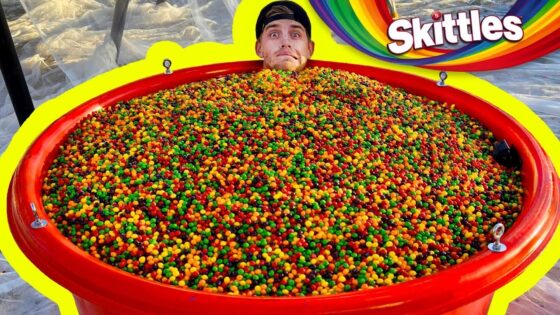 Man's head sticking out from a giant red tub filled with multicolored Skittles candy, with a bright yellow border and Skittles logo in the background.