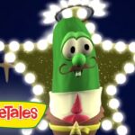 Green cucumber VeggieTales character with a mustache and halo, posed in front of a glowing star-shaped light backdrop with the VeggieTales logo in the corner.
