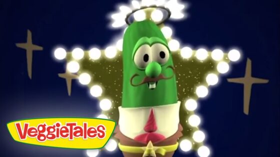 Green cucumber VeggieTales character with a mustache and halo, posed in front of a glowing star-shaped light backdrop with the VeggieTales logo in the corner.