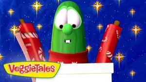 Larry the Cucumber from VeggieTales wearing a red scarf, with two red gift tubes against a blue starry background, logo bottom left.