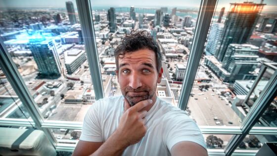 Man taking a selfie on a glass-walled observation deck with a city skyline below