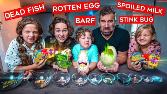 Family of five posing with gross-food challenge props labeled Dead Fish, Rotten Egg, Spoiled Milk, Barf, and Stink Bug; bowls of jelly beans in front.