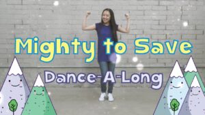 Young woman in a blue dress dances with arms raised in front of a gray brick wall, with colorful mountains and the title 'Mighty to Save Dance-A-Long' on the sides.