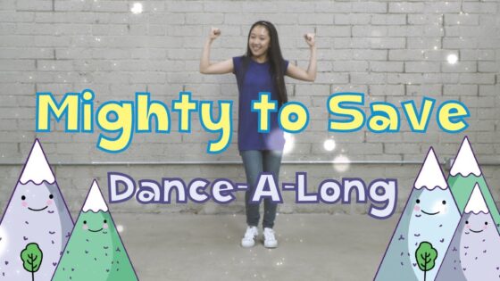 Young woman in a blue dress dances with arms raised in front of a gray brick wall, with colorful mountains and the title 'Mighty to Save Dance-A-Long' on the sides.