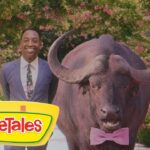 Smiling man in a blue suit stands beside a large buffalo wearing a pink bow tie, with a VeggieTales logo in the foreground and a floral backdrop.