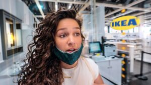 Woman with a teal mask pulled down under her chin stands at a store checkout area inside IKEA.