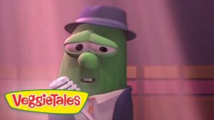 Green veggie character in a suit and hat sings into a microphone on a stage, VeggieTales logo in the corner.