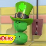 Stacked green veggie characters from VeggieTales wearing a leprechaun hat with a four-leaf clover, next to a wall switch on pastel tiled wall.