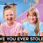 Two smiling girls in pink and blue shirts laugh in a bright, pastel-colored room; bold caption at the bottom asks 'HAVE YOU EVER STOLEN?'.,