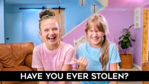 Two smiling girls in pink and blue shirts laugh in a bright, pastel-colored room; bold caption at the bottom asks 'HAVE YOU EVER STOLEN?'.,