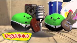 Two green VeggieTales characters perform on a wooden stage with a mic and guitar; VeggieTales logo in the corner.