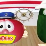 Two VeggieTales characters, a red tomato and a green cucumber, on a ship deck with a steering wheel and logo in the foreground.
