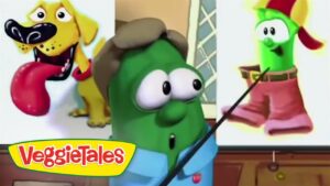 Green VeggieTales host with a pointer, shown with a split-screen slide of a dog on the left and a hat-wearing green veggie on the right.