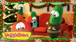 Three VeggieTales characters—Tomato, Broccoli with a scarf, and a green cucumber in a holiday sweater—sit on a couch in a festively decorated living room with a Christmas tree in the background.