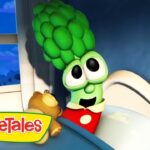 Larry the Cucumber from VeggieTales sits up in bed with a brown teddy bear in a blue bedroom; VeggieTales logo in the corner.